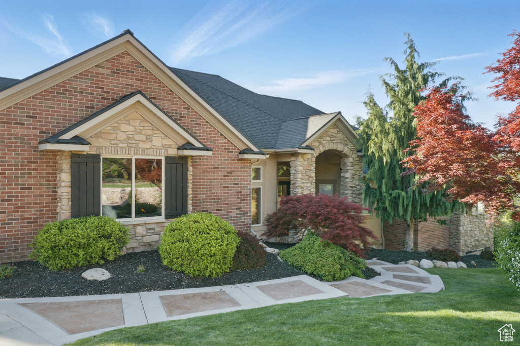 View of front facade with stone siding, a front yard, a shingled roof, and brick siding