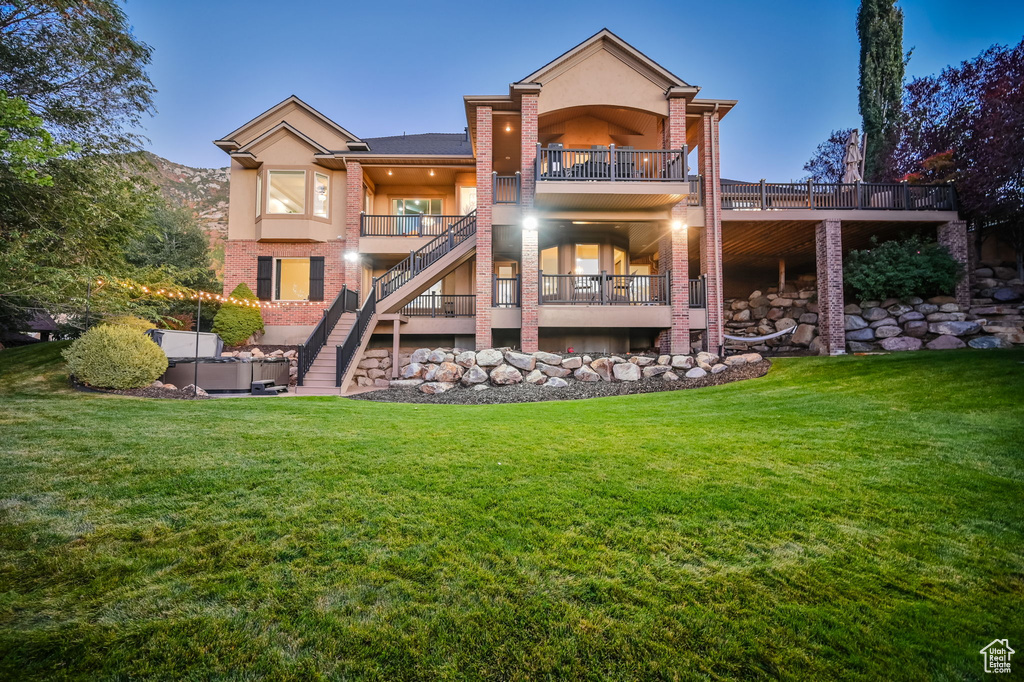 Back of property with stairway, brick siding, a balcony, a yard, and stucco siding