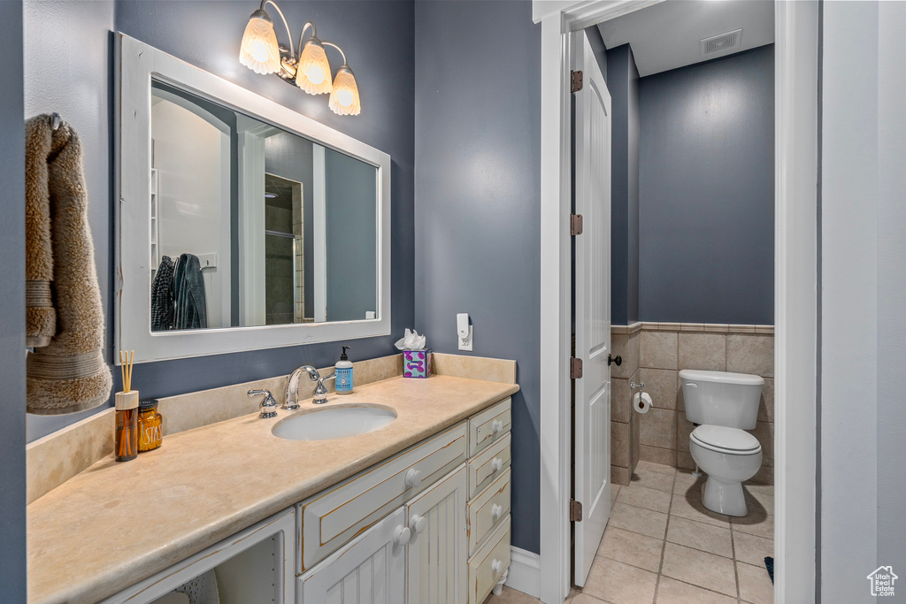Bathroom featuring tile patterned flooring, toilet, tile walls, vanity, and wainscoting