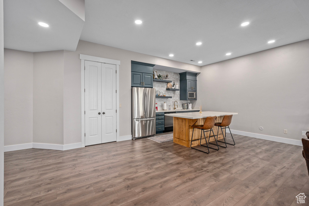 Kitchen with appliances with stainless steel finishes, open shelves, light countertops, wood finished floors, and tasteful backsplash