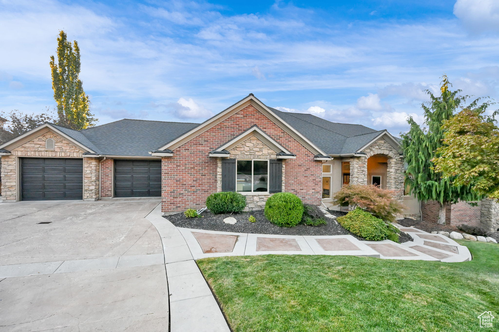 View of front of property featuring an attached garage, stone siding, driveway, a front lawn, and a shingled roof