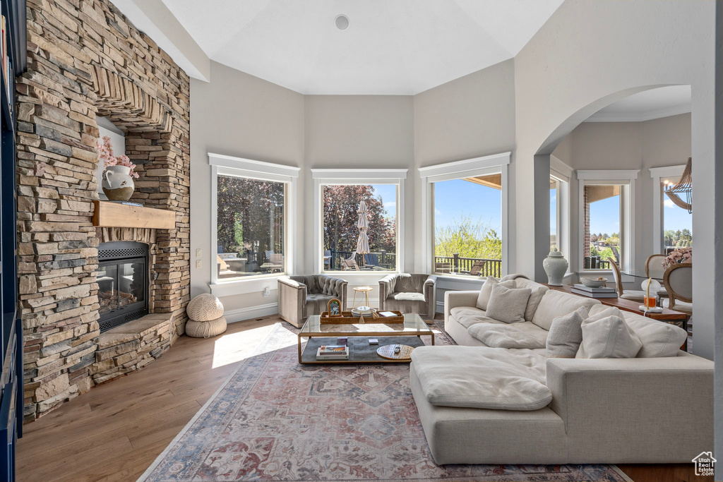 Living area with a stone fireplace, wood finished floors, high vaulted ceiling, and arched walkways