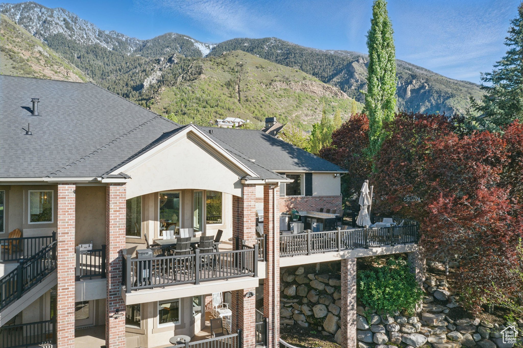 Back of house featuring brick siding, a mountain view, a shingled roof, and a balcony