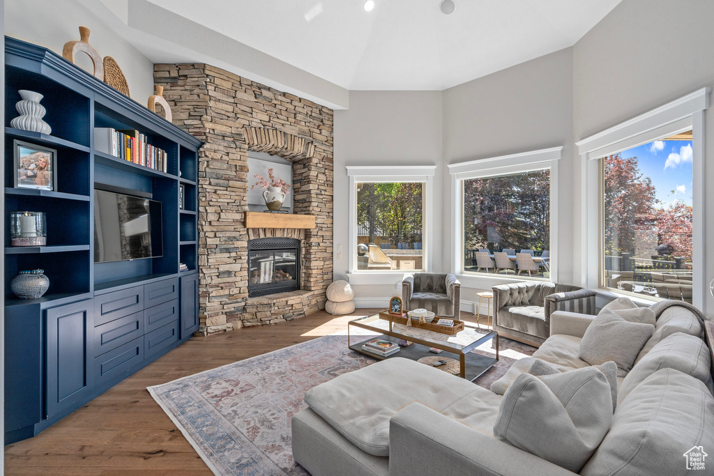 Living room with a towering ceiling, a stone fireplace, and wood finished floors