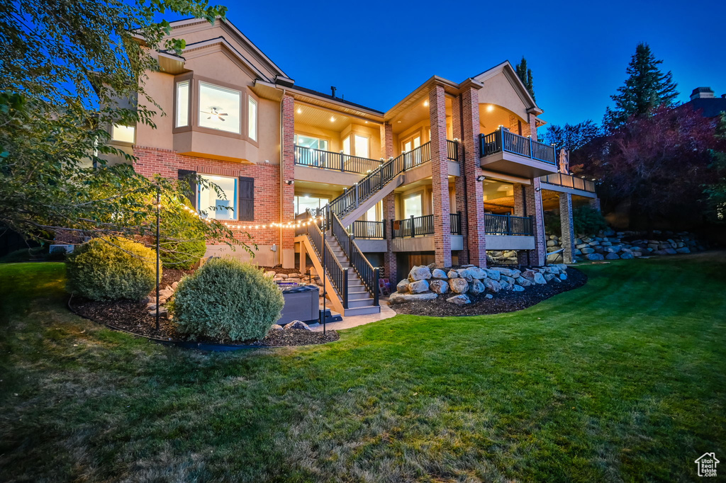 Rear view of house featuring brick siding, stucco siding, a balcony, and a lawn