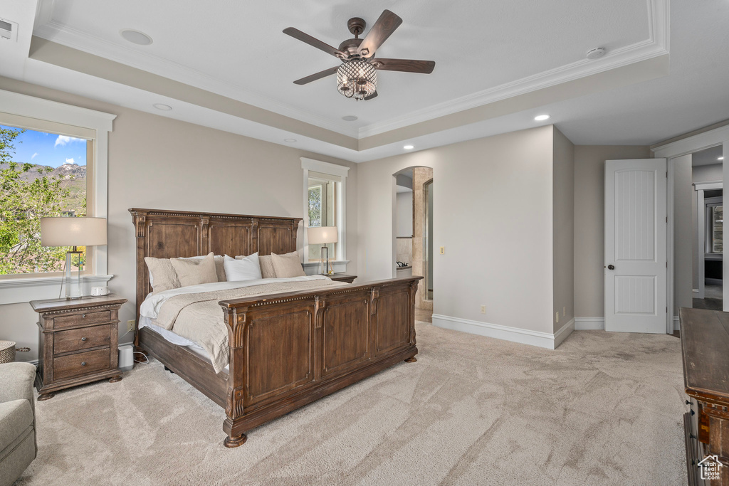 Bedroom with a tray ceiling, light carpet, crown molding, multiple windows, and recessed lighting