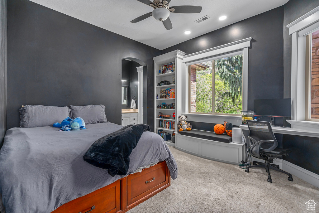 Carpeted bedroom with arched walkways, connected bathroom, a ceiling fan, a desk, and recessed lighting