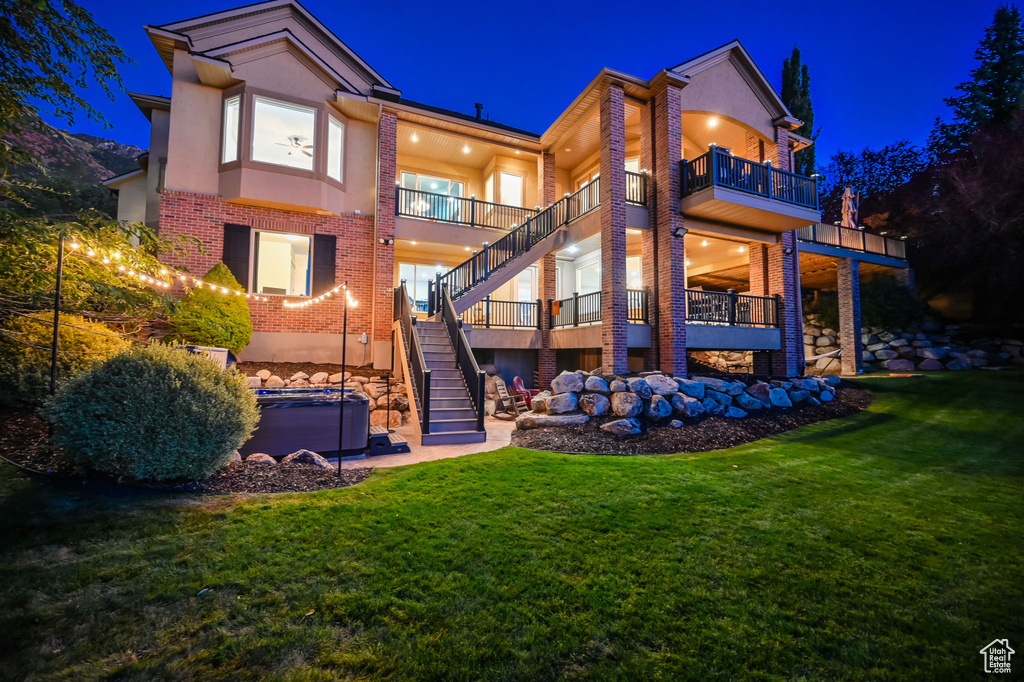 Back of house at twilight featuring stucco siding, brick siding, stairway, and a lawn