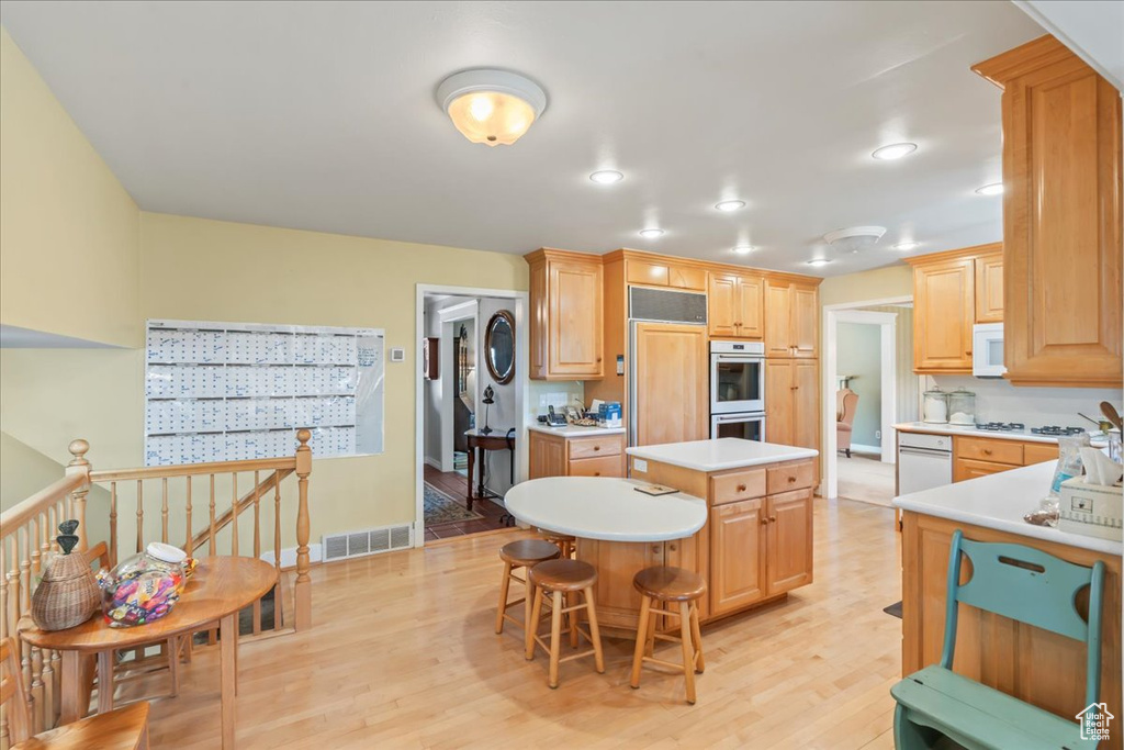 Kitchen with a center island, white appliances, light countertops, light wood-type flooring, and a breakfast bar area