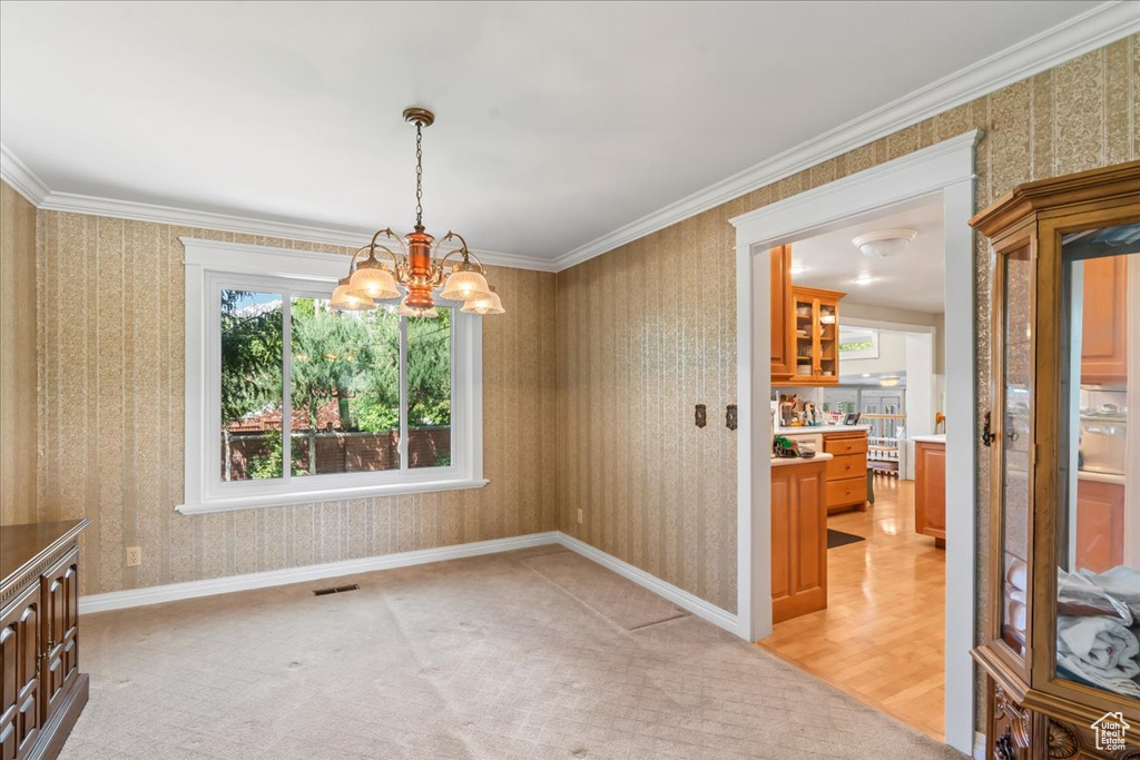 Unfurnished dining area with wallpapered walls, a chandelier, light colored carpet, and crown molding