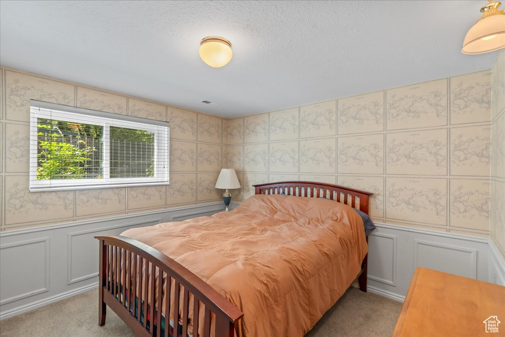 Bedroom with a decorative wall, light carpet, and a wainscoted wall