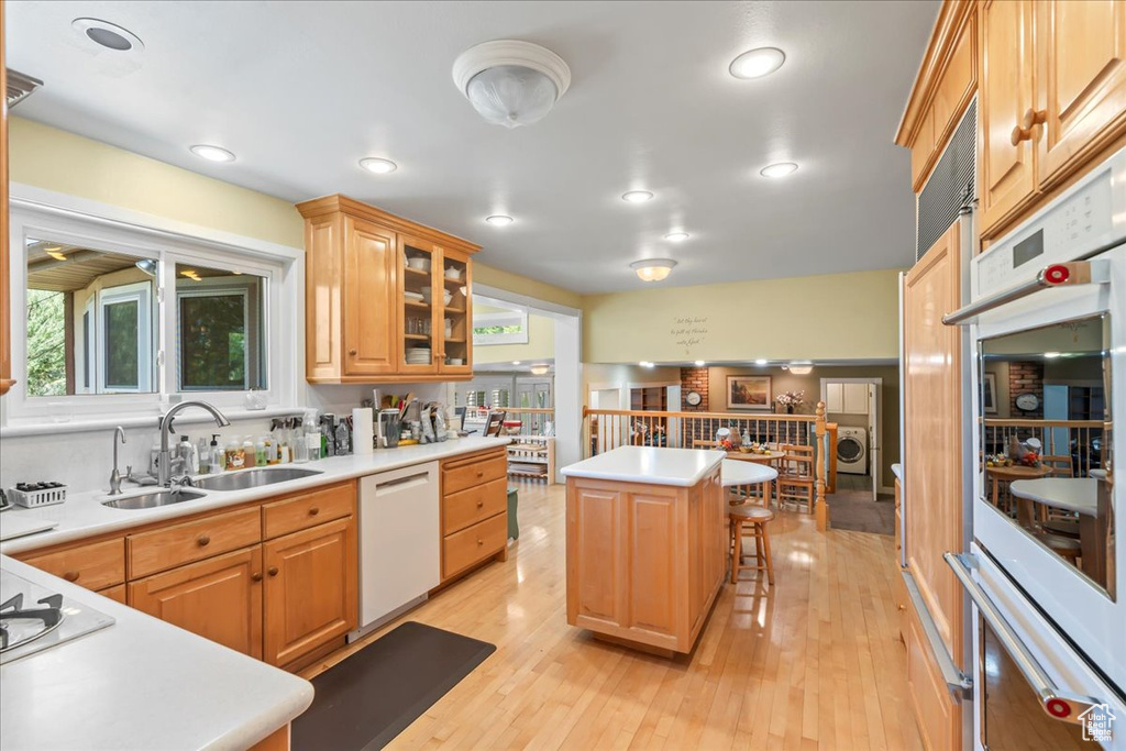 Kitchen with white appliances, a sink, a kitchen bar, a center island, and light countertops