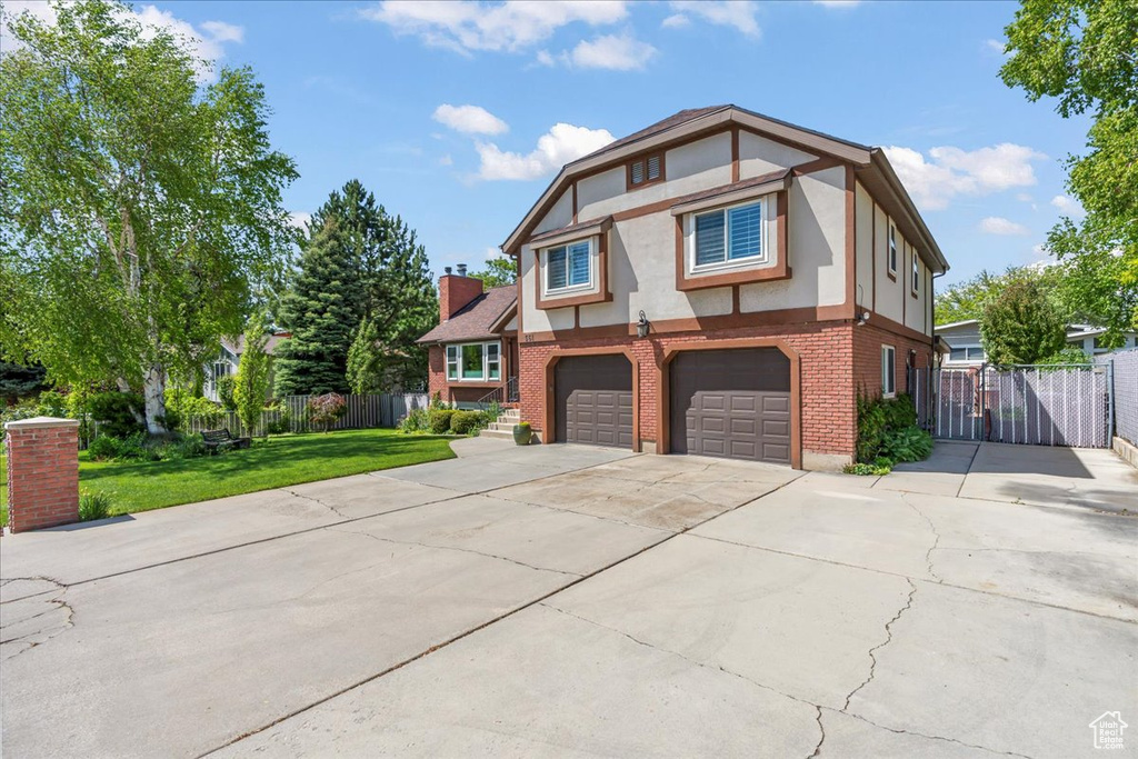 English style home with stucco siding, brick siding, concrete driveway, a garage, and a gate