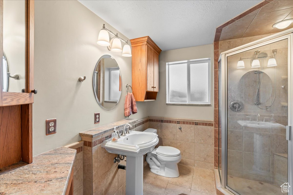 Bathroom featuring a shower stall, a textured ceiling, tile patterned flooring, tile walls, and toilet
