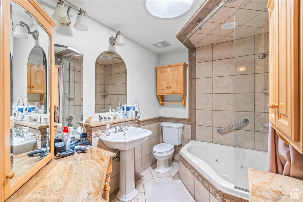 Bathroom with a whirlpool tub, tile walls, tile patterned flooring, a sink, and toilet
