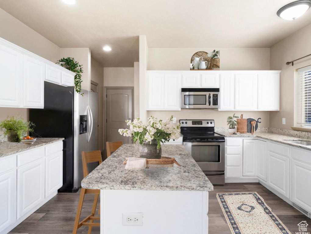Kitchen featuring a breakfast bar, white cabinetry, dark wood-type flooring, appliances with stainless steel finishes, and a kitchen island