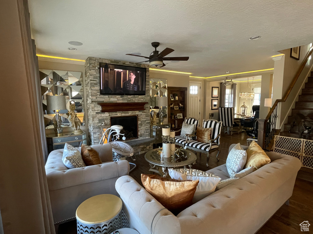 Living area with a ceiling fan, wood finished floors, crown molding, a stone fireplace, and stairs