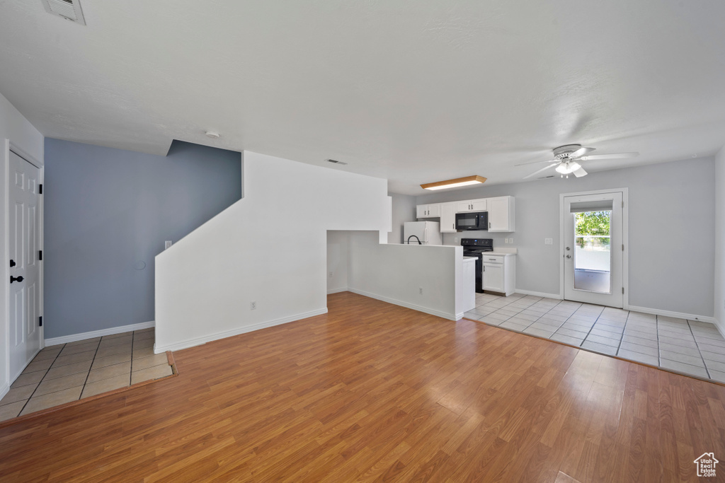 Unfurnished living room featuring light wood finished floors, ceiling fan, and baseboards