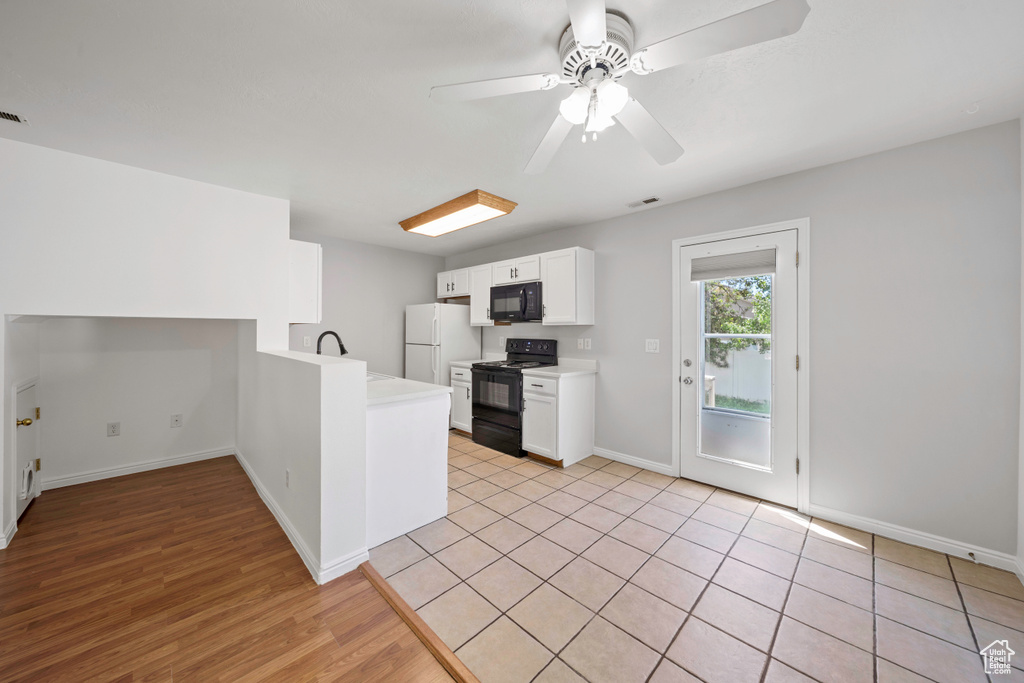 Kitchen with black appliances, a peninsula, light countertops, baseboards, and white cabinets