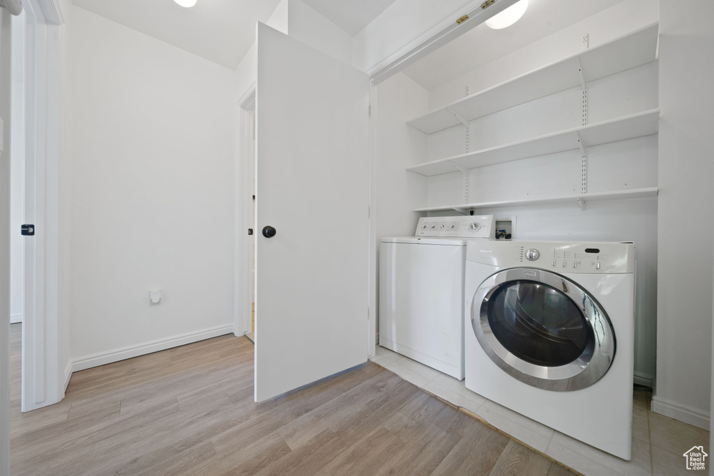 Laundry area featuring washer and clothes dryer, light wood-style floors, and baseboards
