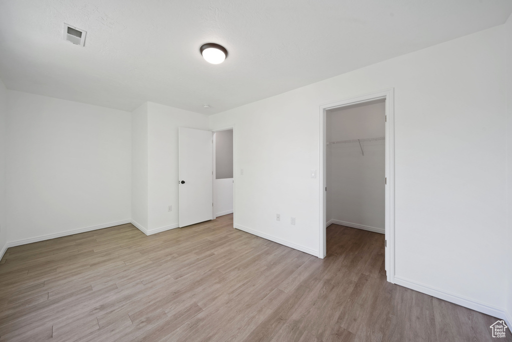 Unfurnished bedroom featuring light wood-style flooring, baseboards, a walk in closet, and a closet