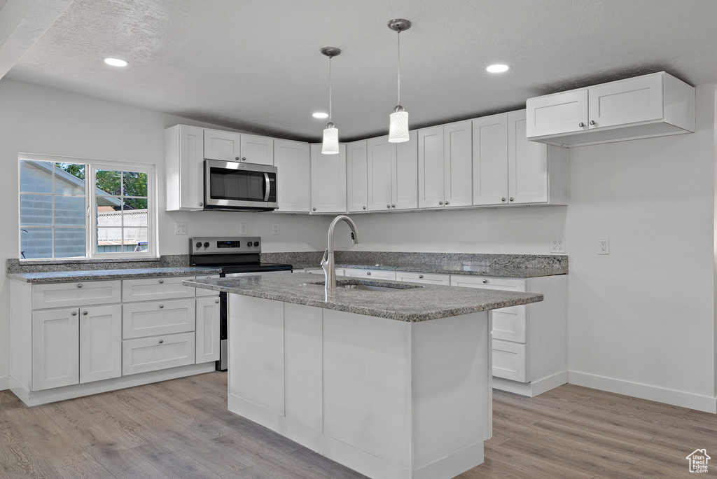 Kitchen featuring stainless steel appliances, a sink, light wood-type flooring, light stone countertops, and white cabinets