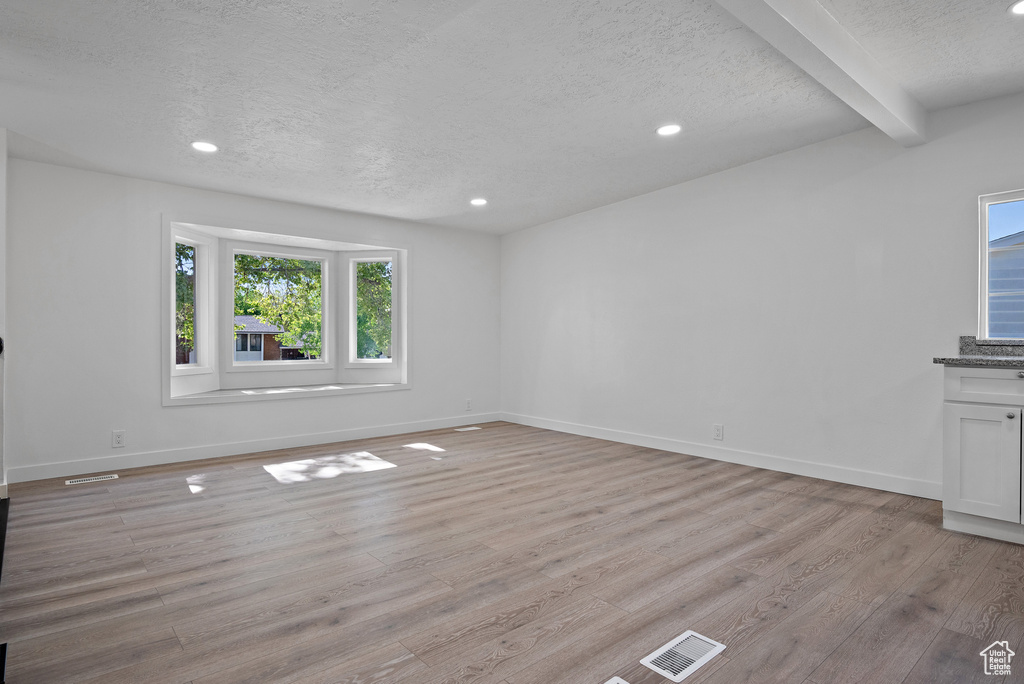 Unfurnished living room with a textured ceiling, light wood-style floors, recessed lighting, baseboards, and beamed ceiling