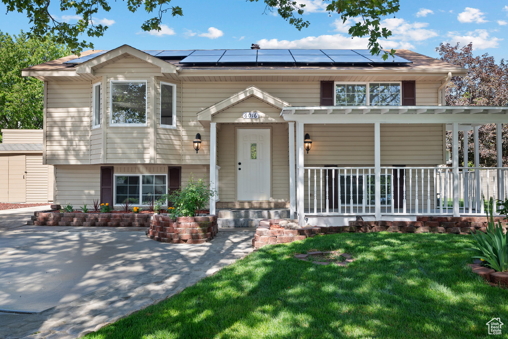 View of front of home with covered porch, solar panels, and a front yard