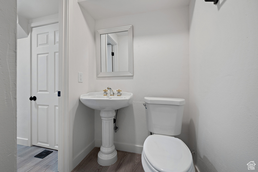 Half bathroom with toilet, wood finished floors, and baseboards