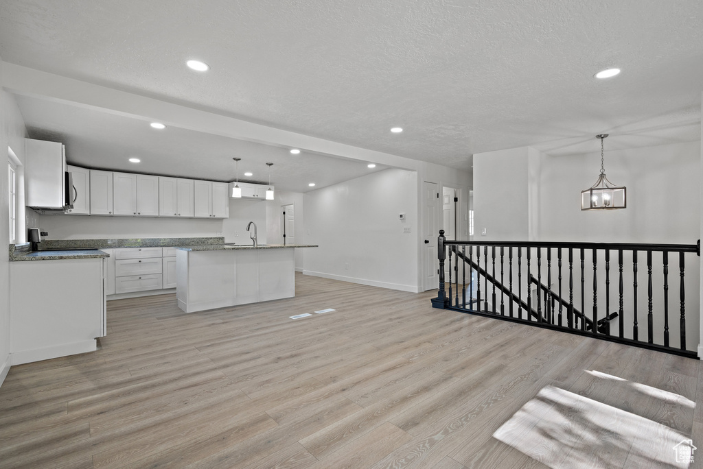 Kitchen featuring recessed lighting, white cabinetry, light wood-style floors, a kitchen island with sink, and decorative light fixtures
