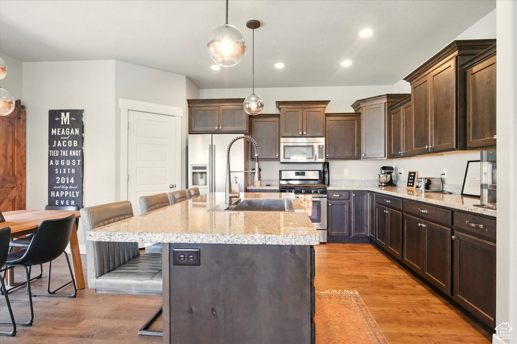 Kitchen featuring stainless steel appliances, dark brown cabinets, a kitchen bar, a sink, and recessed lighting