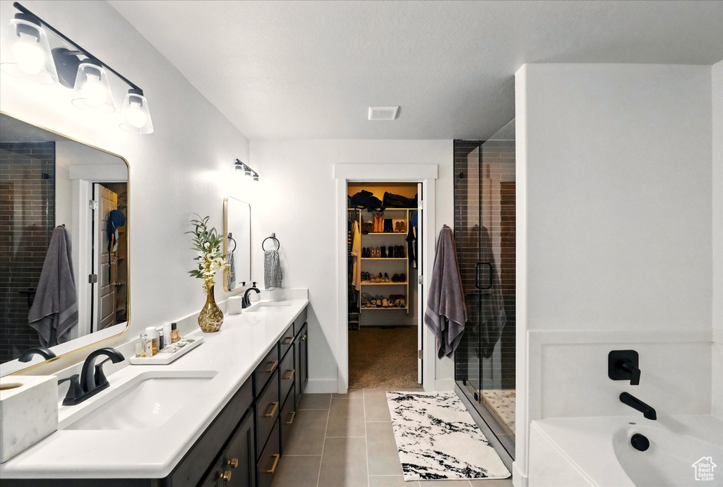 Bathroom featuring tile patterned floors, a shower stall, a walk in closet, double vanity, and a tub to relax in