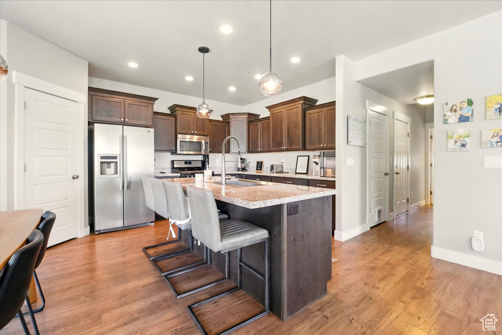 Kitchen with stainless steel appliances, a sink, a kitchen island with sink, dark brown cabinetry, and recessed lighting