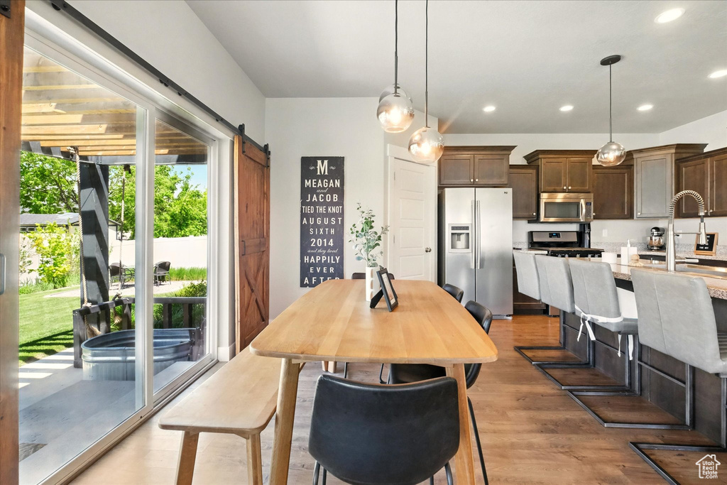 Dining area with a barn door, light wood-type flooring, and recessed lighting