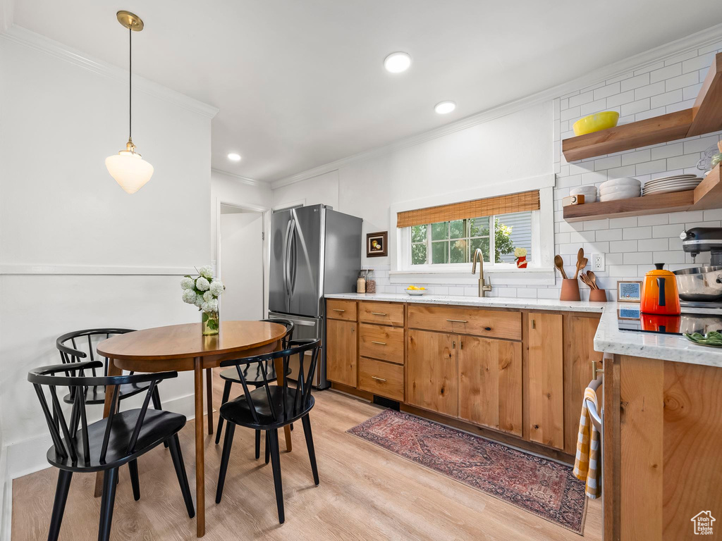 Kitchen featuring freestanding refrigerator, a sink, crown molding, decorative backsplash, and light wood-style floors