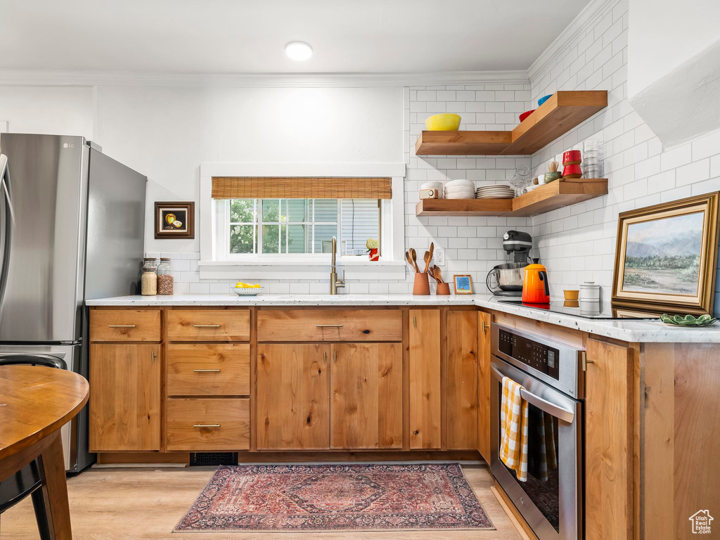 Kitchen with stainless steel appliances, ornamental molding, a sink, light wood-type flooring, and tasteful backsplash