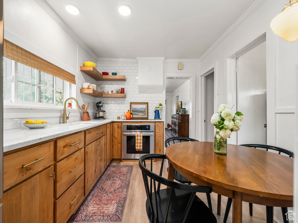 Kitchen featuring oven, a sink, crown molding, light wood-type flooring, and backsplash