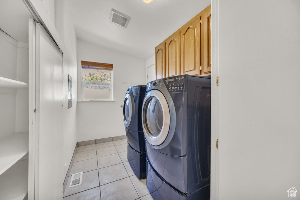 Washroom featuring washing machine and dryer, cabinet space, light tile patterned flooring, and baseboards