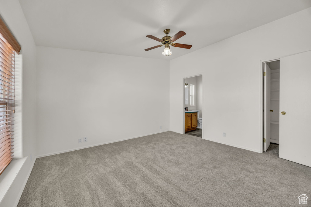 Unfurnished bedroom featuring carpet, a walk in closet, connected bathroom, and ceiling fan