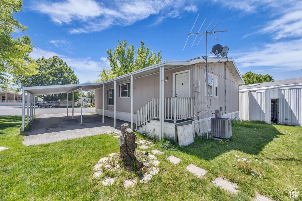 Back of house featuring a lawn, central AC unit, and an attached carport