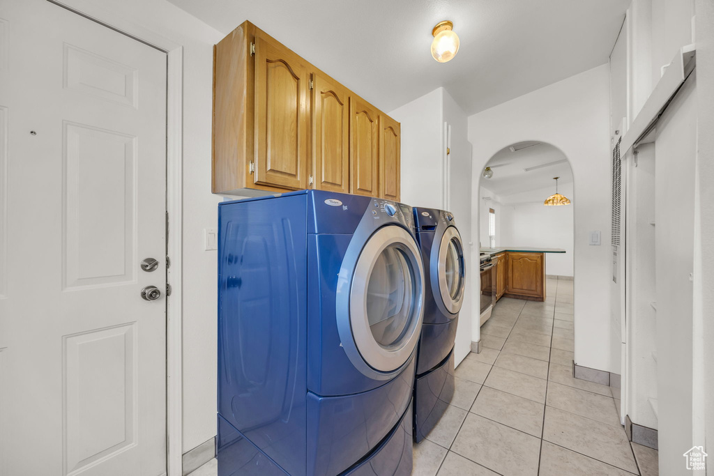 Laundry room with washing machine and dryer, arched walkways, light tile patterned floors, and cabinet space