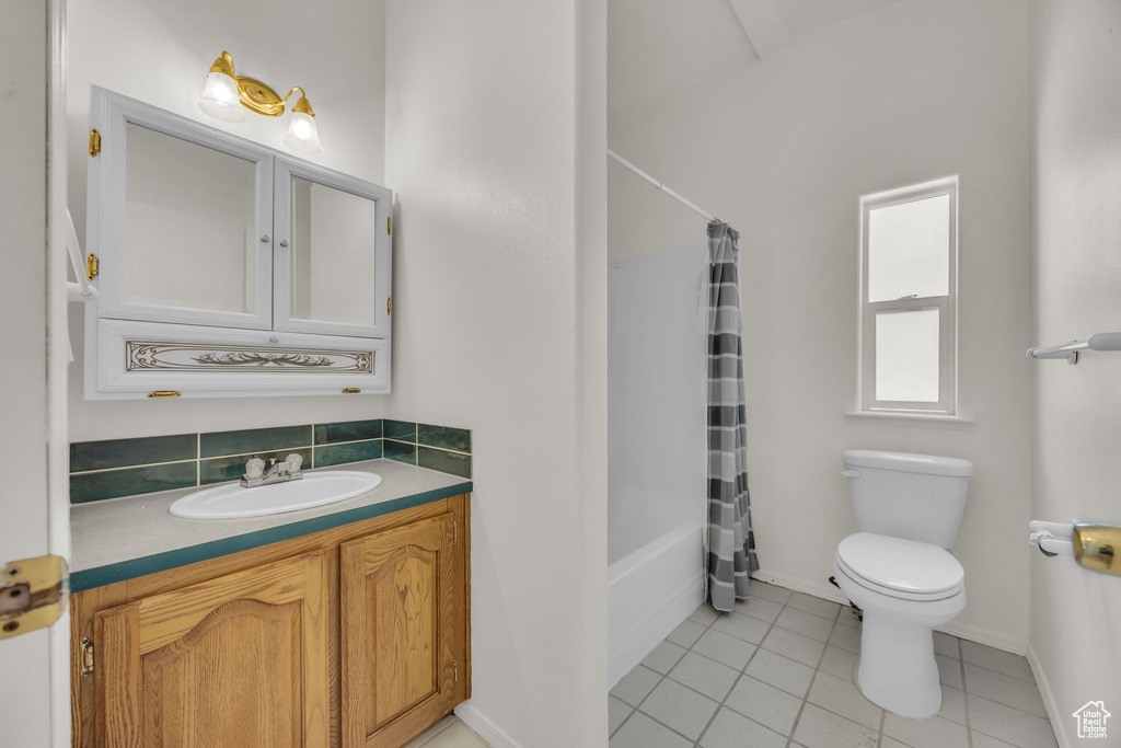 Full bath with toilet, tile patterned floors, vanity, shower / bath combination with curtain, and baseboards