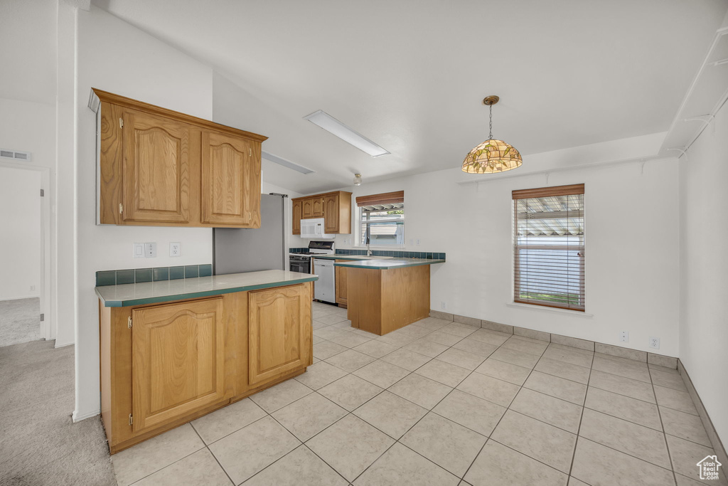 Kitchen featuring freestanding refrigerator, a peninsula, white microwave, range, and hanging light fixtures