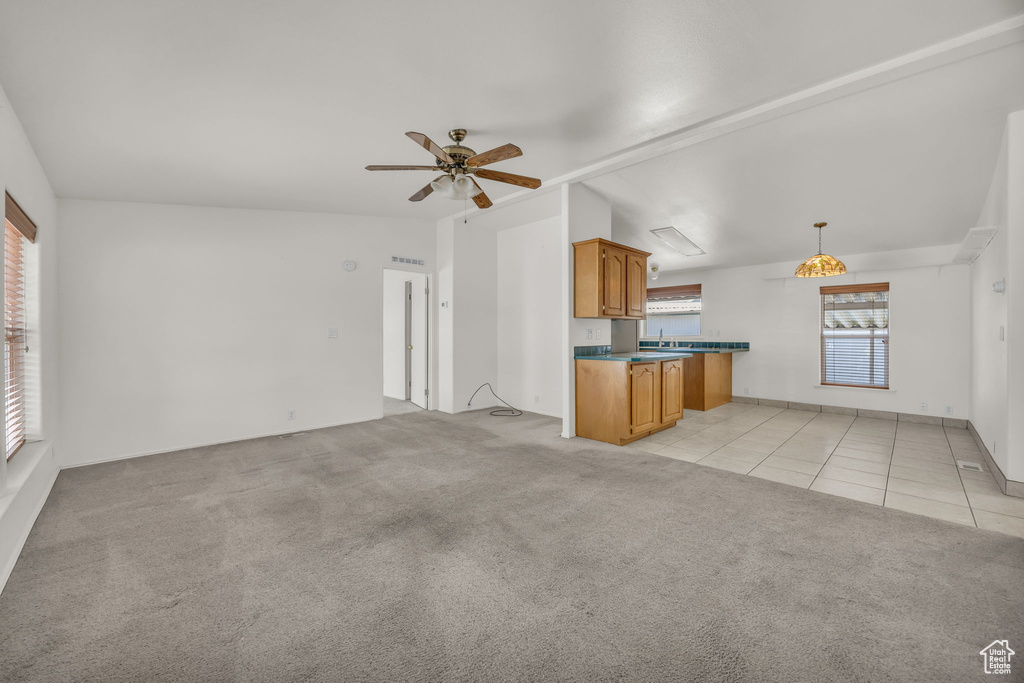 Kitchen featuring light colored carpet, brown cabinets, ceiling fan, light tile patterned floors, and open floor plan
