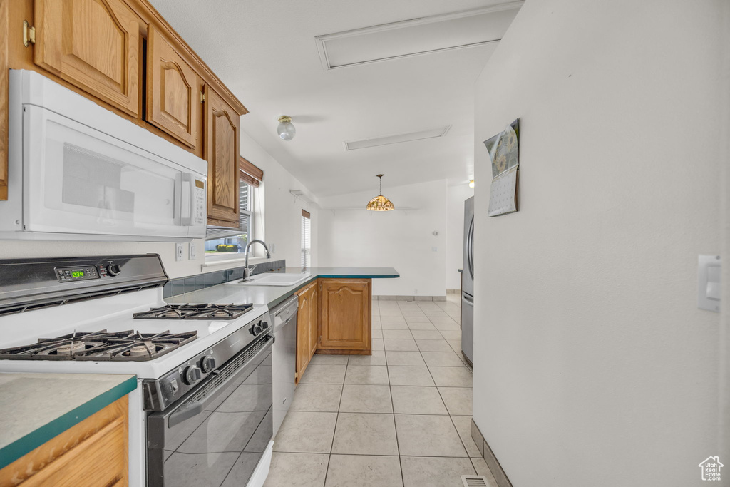 Kitchen featuring appliances with stainless steel finishes, a peninsula, a sink, light tile patterned flooring, and hanging light fixtures