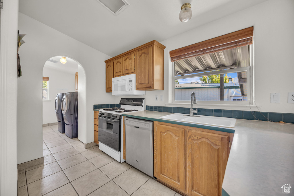 Kitchen with white appliances, washing machine and clothes dryer, a sink, arched walkways, and light tile patterned floors