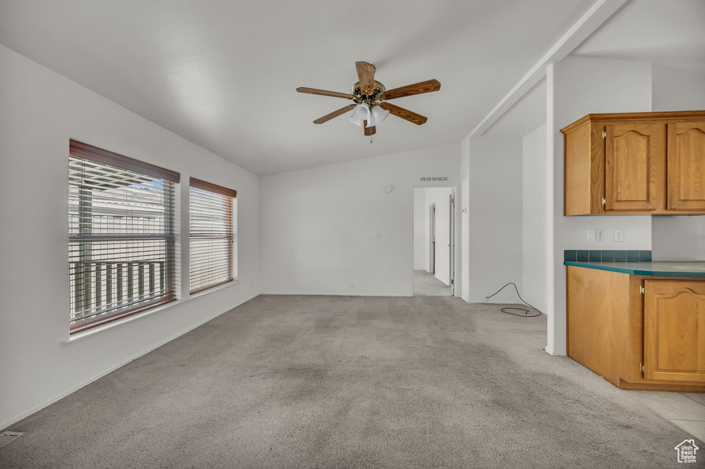 Unfurnished living room featuring lofted ceiling, a ceiling fan, and light colored carpet