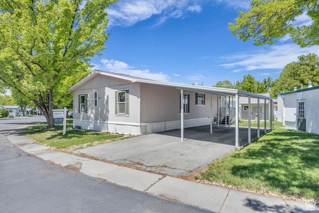 Manufactured / mobile home with a front yard, asphalt driveway, and an attached carport