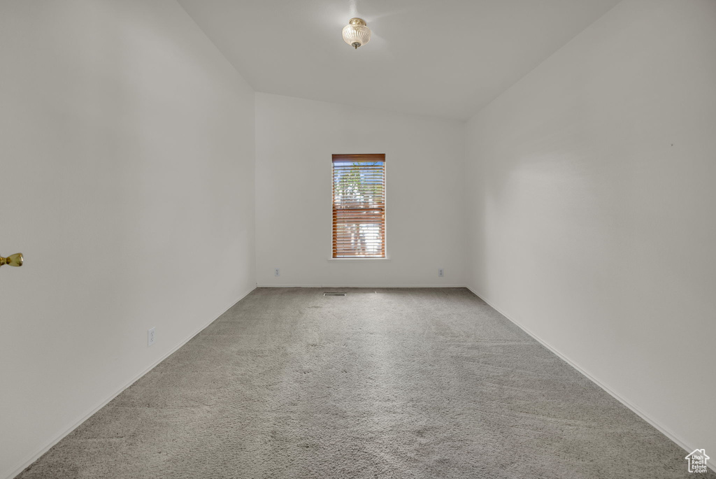Carpeted spare room featuring vaulted ceiling