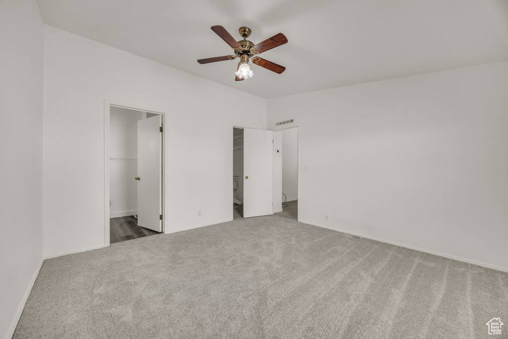 Unfurnished bedroom with carpet floors, a walk in closet, baseboards, ensuite bathroom, and ceiling fan